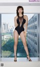 A woman in a black swimsuit posing in front of a window.