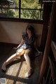 A woman sitting on a wooden floor in front of a window.