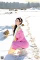 A woman in a pink dress crouching down in the snow.