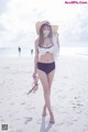 A woman in a bikini and hat walking on the beach.