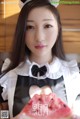 A woman in a maid outfit holding a slice of watermelon.