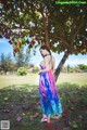 A woman in a colorful dress standing under a tree.