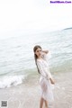 A woman in a white dress standing on the beach.