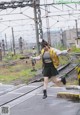 A woman in a yellow jacket and black skirt is jumping on a train track.